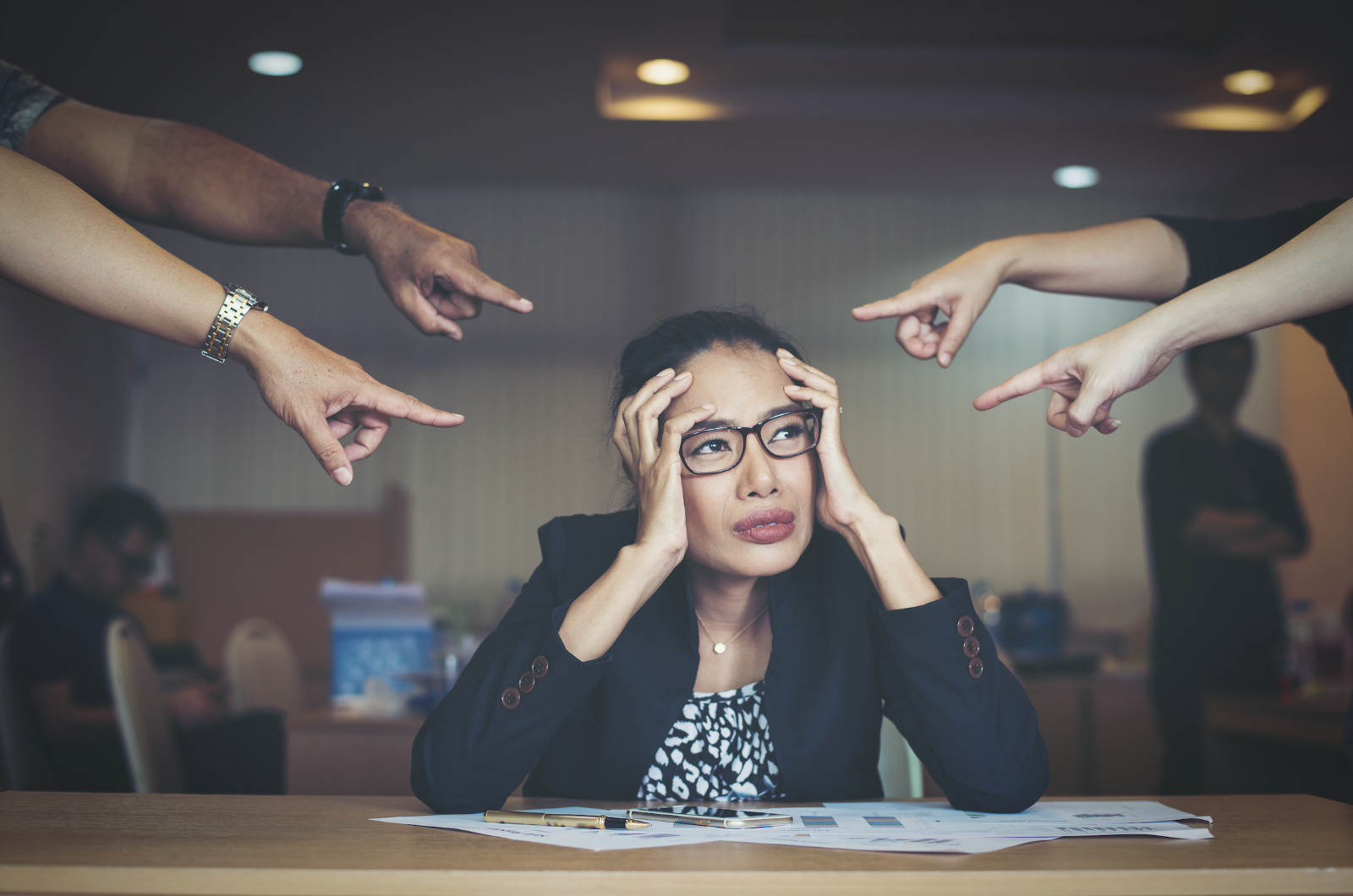 A person sitting at a table with hands pointing at her headDescription automatically generated